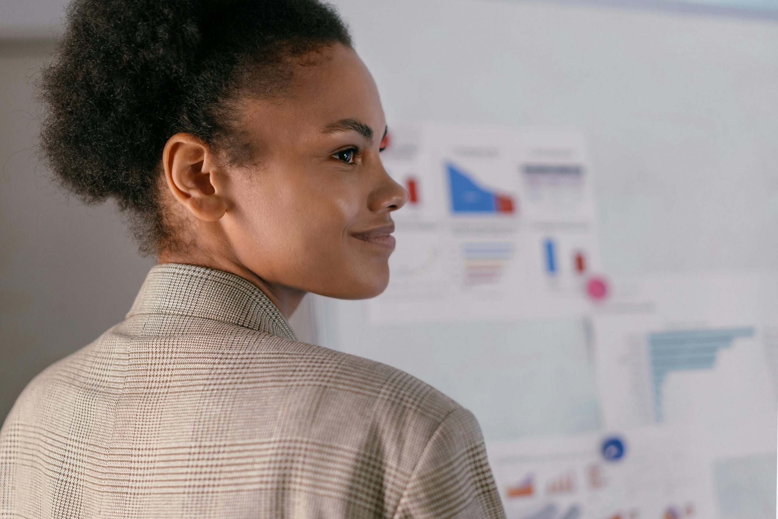 smiling woman in a blazer, with a whiteboard full of charts in the background
