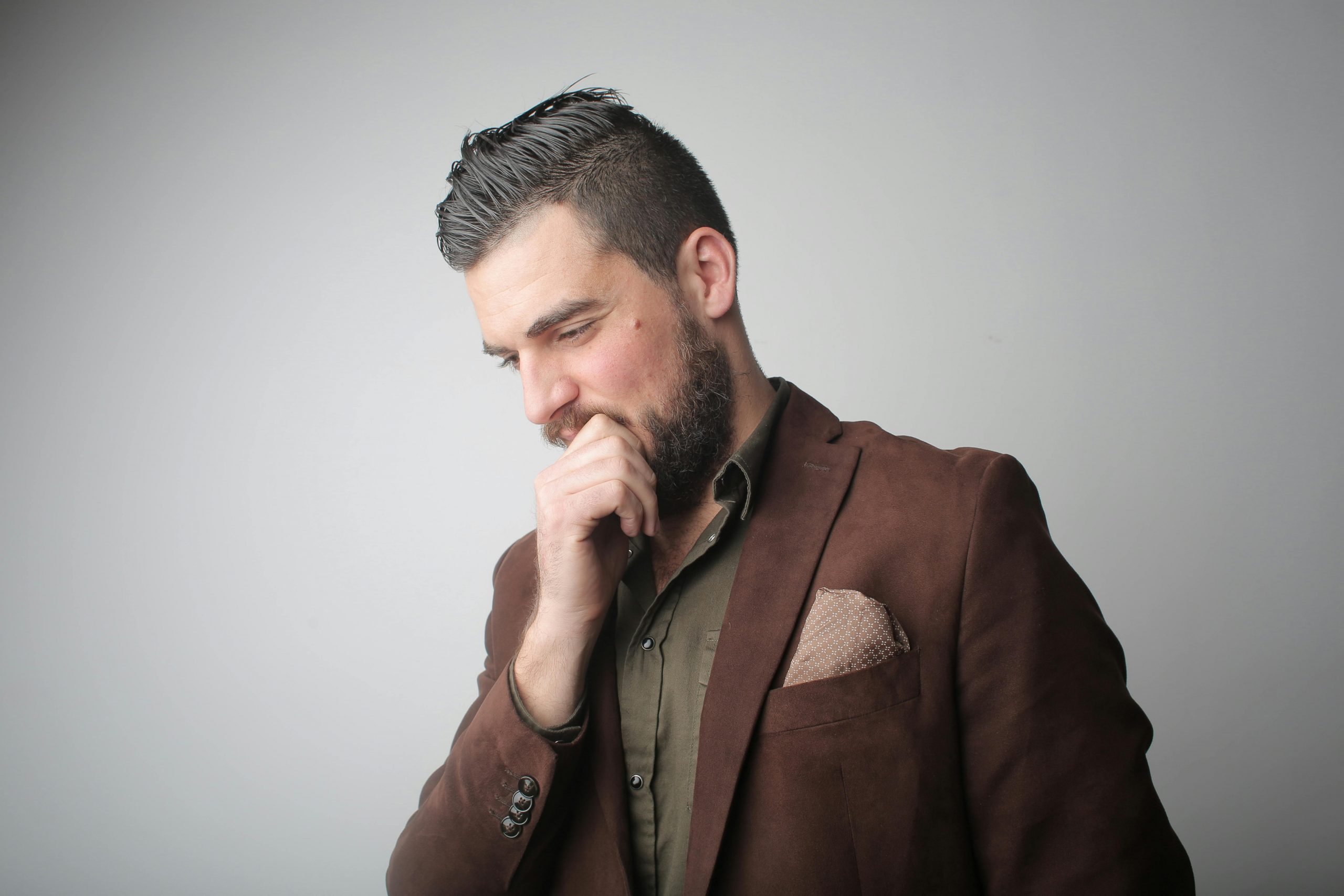 man in a brown suit with his chin resting on his hand