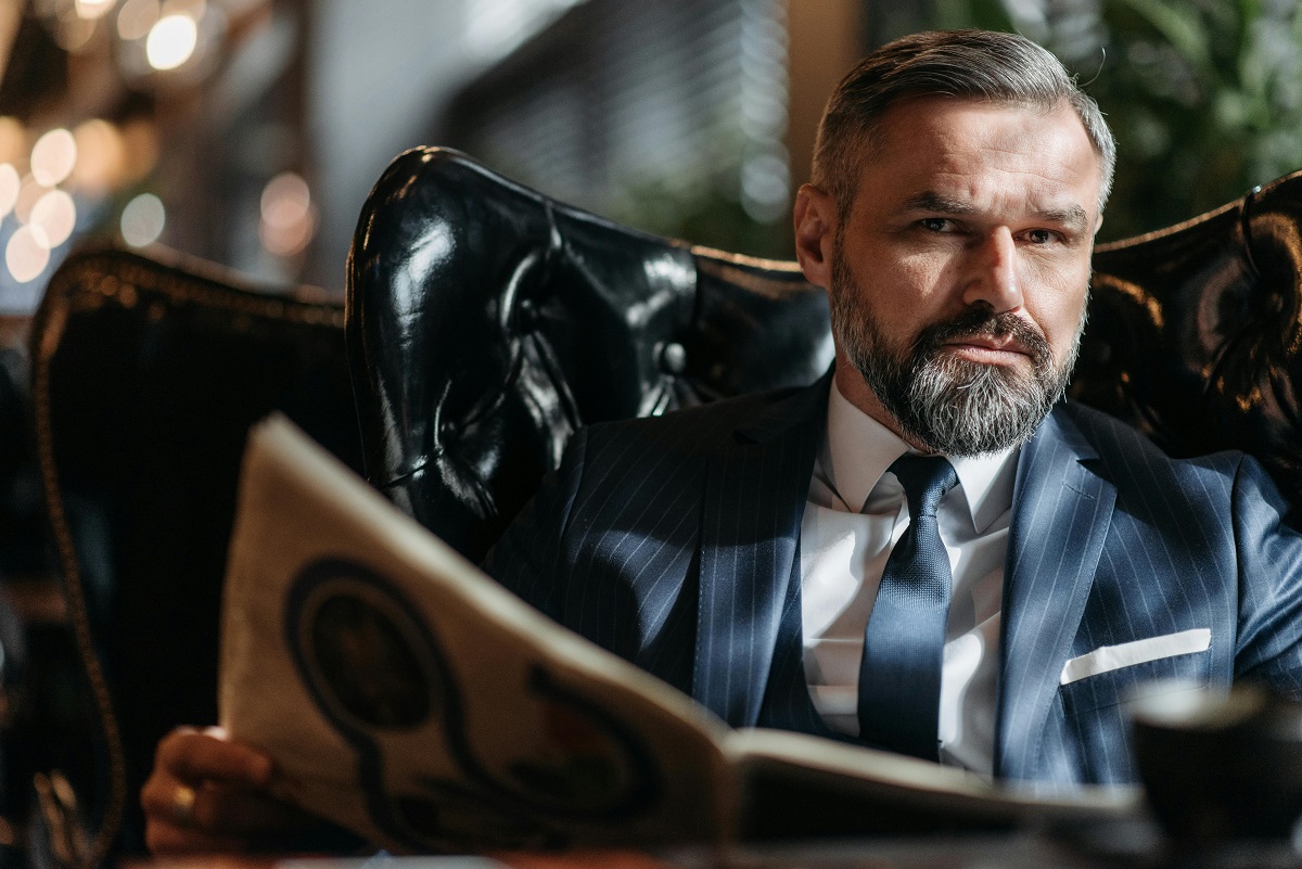 man in a pin-stripe suit seated, holding an open book